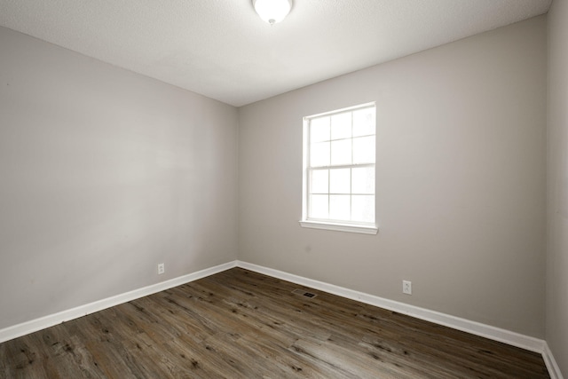 empty room featuring dark wood finished floors, baseboards, and visible vents