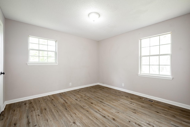 empty room featuring baseboards, visible vents, wood finished floors, and a textured ceiling