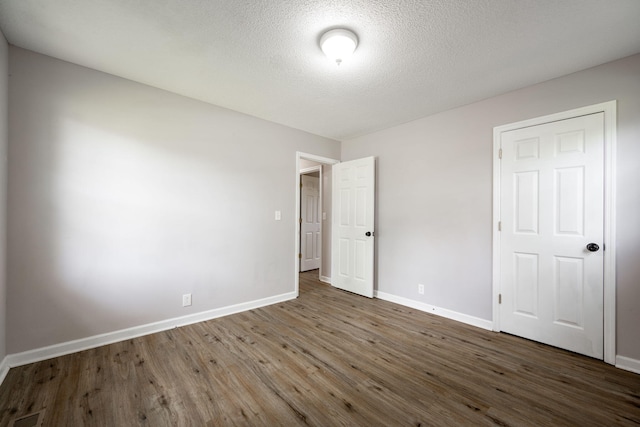 unfurnished bedroom with wood finished floors, a textured ceiling, baseboards, and visible vents