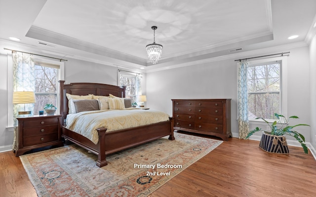 bedroom with visible vents, a tray ceiling, multiple windows, and wood finished floors