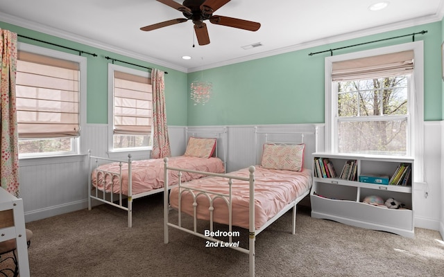 bedroom featuring ornamental molding, a ceiling fan, a wainscoted wall, visible vents, and carpet