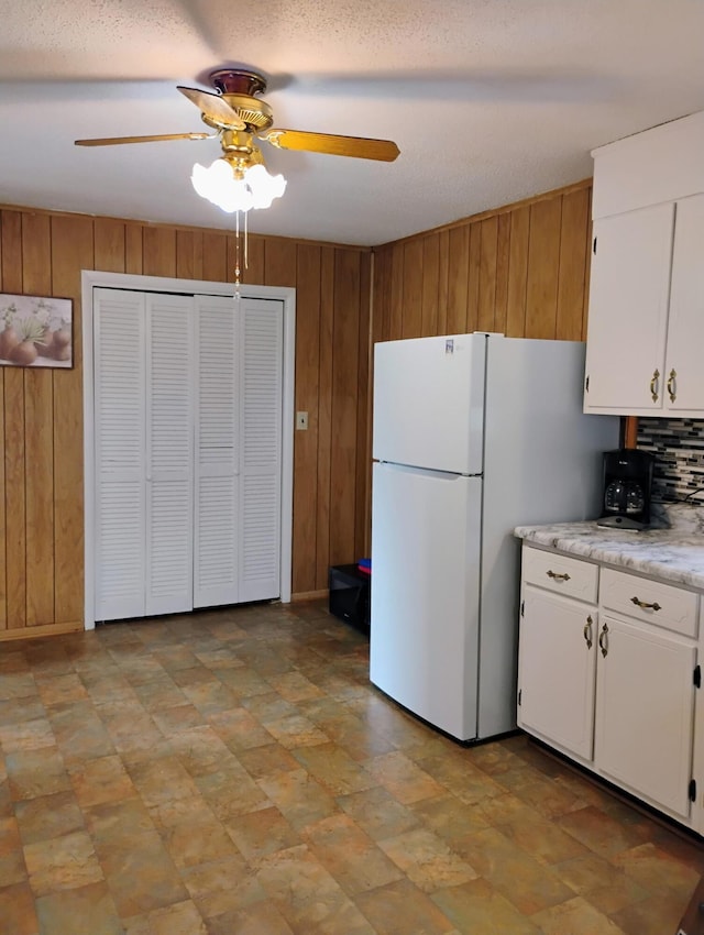 kitchen with freestanding refrigerator, light countertops, wood walls, white cabinetry, and a ceiling fan