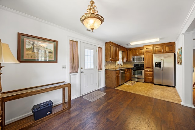 kitchen featuring stainless steel appliances, brown cabinetry, ornamental molding, and wood finished floors
