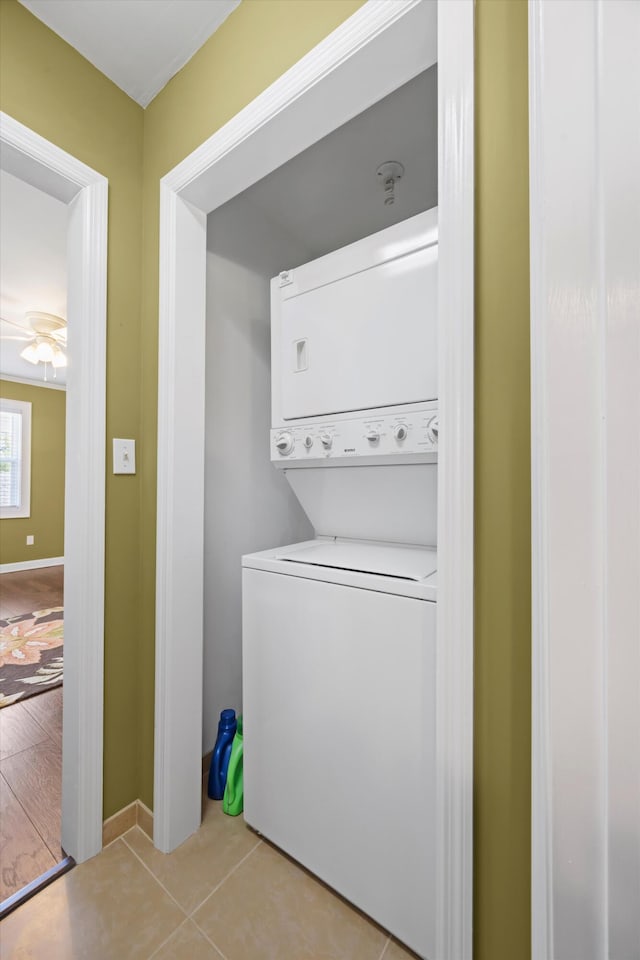 laundry area featuring laundry area, a ceiling fan, stacked washer / dryer, light tile patterned flooring, and baseboards