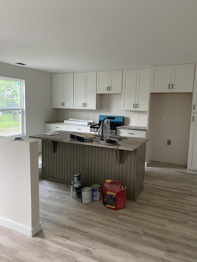 kitchen featuring white cabinets, light wood-style flooring, a center island, a sink, and baseboards