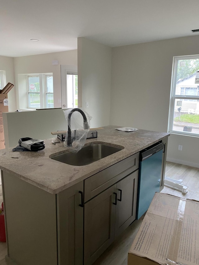 kitchen with a kitchen island with sink, a sink, dishwashing machine, and light wood-type flooring