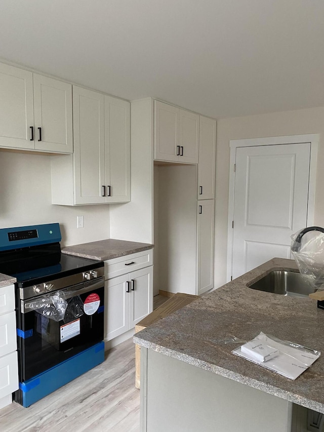 kitchen with light wood finished floors, dark stone countertops, a sink, electric range, and white cabinetry