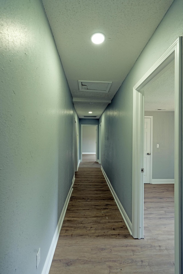hallway with baseboards, attic access, and wood finished floors