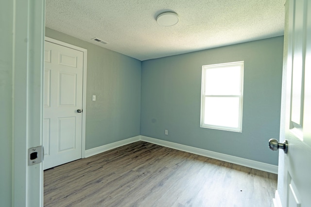 unfurnished room with visible vents, baseboards, wood finished floors, and a textured ceiling