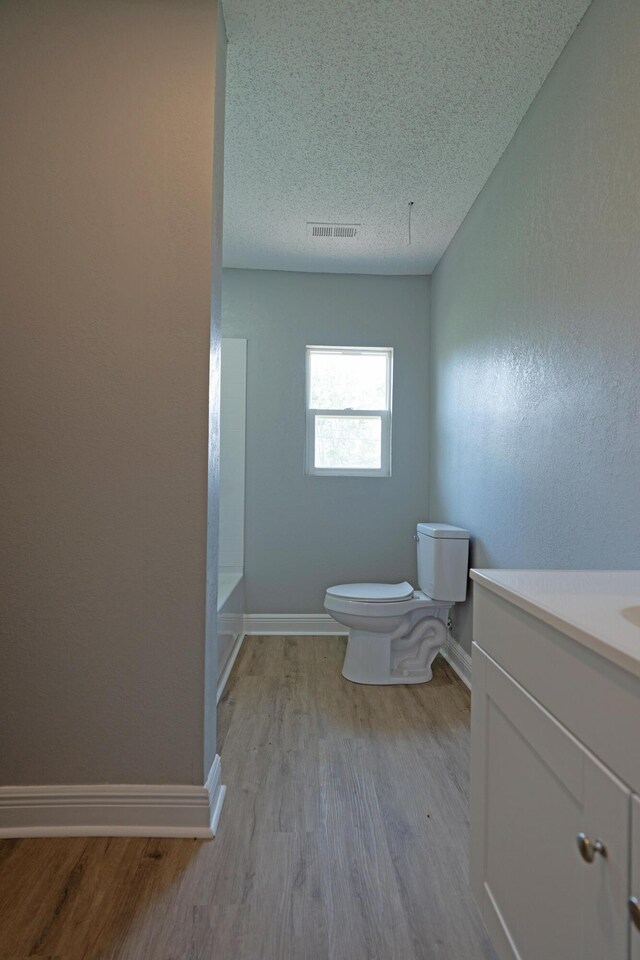 bathroom featuring a textured ceiling, vanity, visible vents, toilet, and wood finished floors