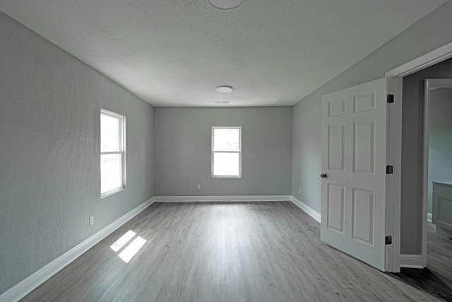 spare room with a textured wall, a textured ceiling, baseboards, and wood finished floors