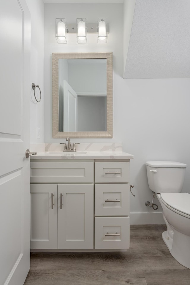 bathroom with toilet, vanity, wood finished floors, and baseboards