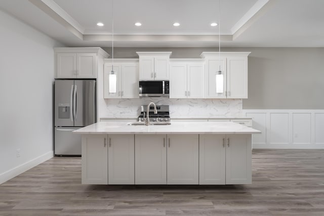 kitchen featuring stainless steel appliances, an island with sink, a sink, and a raised ceiling
