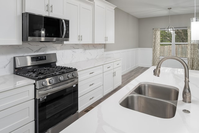 kitchen with white cabinets, wainscoting, stainless steel appliances, a sink, and wood finished floors