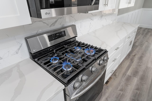 kitchen with white cabinetry, a wainscoted wall, light stone countertops, stainless steel gas stove, and wood finished floors