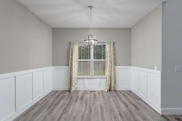 unfurnished dining area featuring a wainscoted wall, an inviting chandelier, and wood finished floors