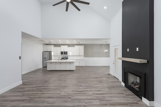 unfurnished living room featuring light wood-type flooring, ceiling fan with notable chandelier, high vaulted ceiling, and a fireplace