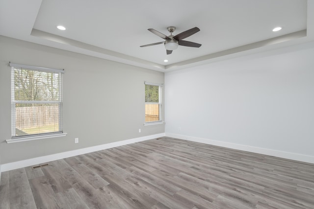 spare room featuring a tray ceiling, wood finished floors, ceiling fan, and baseboards
