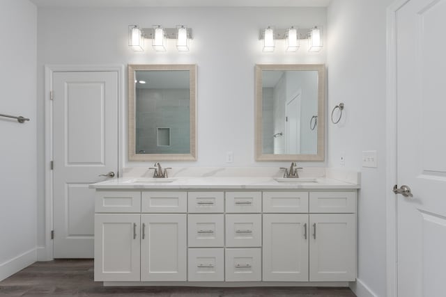 bathroom with double vanity, baseboards, a sink, and wood finished floors