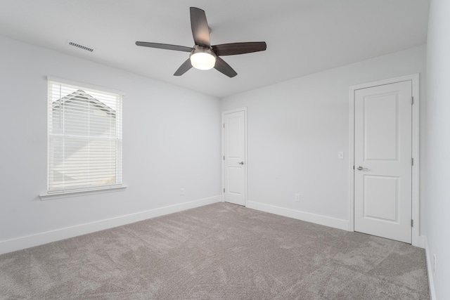 empty room with carpet floors, ceiling fan, visible vents, and baseboards