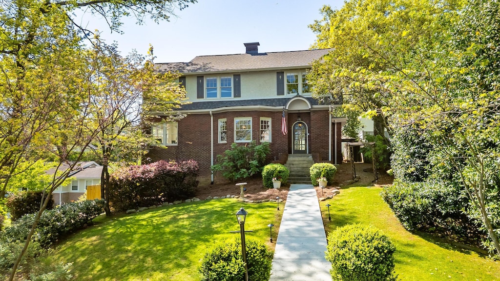 traditional home featuring a front lawn, brick siding, roof with shingles, and a chimney