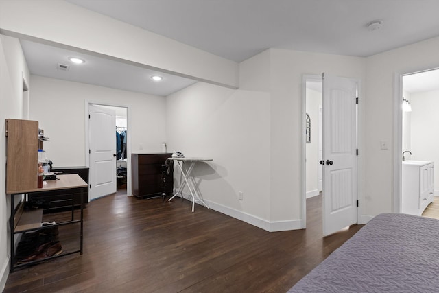 bedroom with ensuite bath, visible vents, wood finished floors, a walk in closet, and baseboards