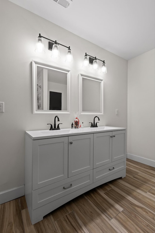 bathroom with a sink, baseboards, double vanity, and wood finished floors