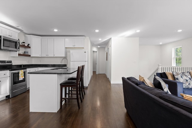 kitchen featuring white cabinetry, dark countertops, a sink, stainless steel appliances, and open floor plan