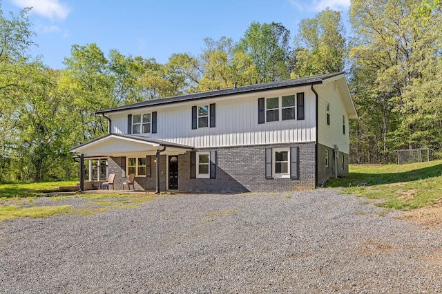 view of front of house featuring a porch, gravel driveway, and brick siding