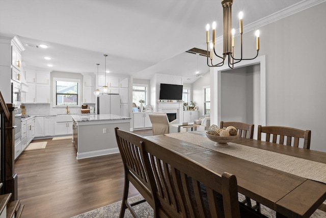 dining space with an inviting chandelier, a fireplace, dark wood-style flooring, ornamental molding, and recessed lighting