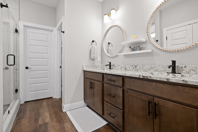 full bathroom featuring baseboards, a sink, a shower stall, double vanity, and wood finished floors
