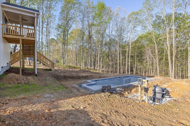 view of pool with a ceiling fan, stairs, an empty pool, and a wooded view