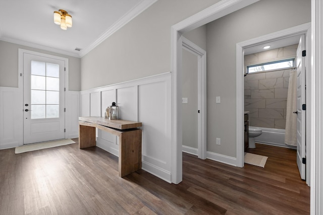 doorway to outside featuring crown molding, visible vents, a decorative wall, wainscoting, and dark wood-style floors
