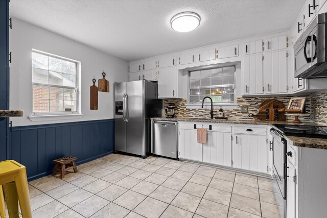 1905 Bella Vista Dr, Chattanooga, TN 37421 - kitchen featuring stainless steel appliances, white cabinets, decorative backsplash, a wainscoted wall, and a textured ceiling