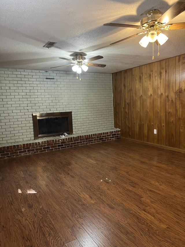 unfurnished living room with wood finished floors, ceiling fan, a brick fireplace, and visible vents