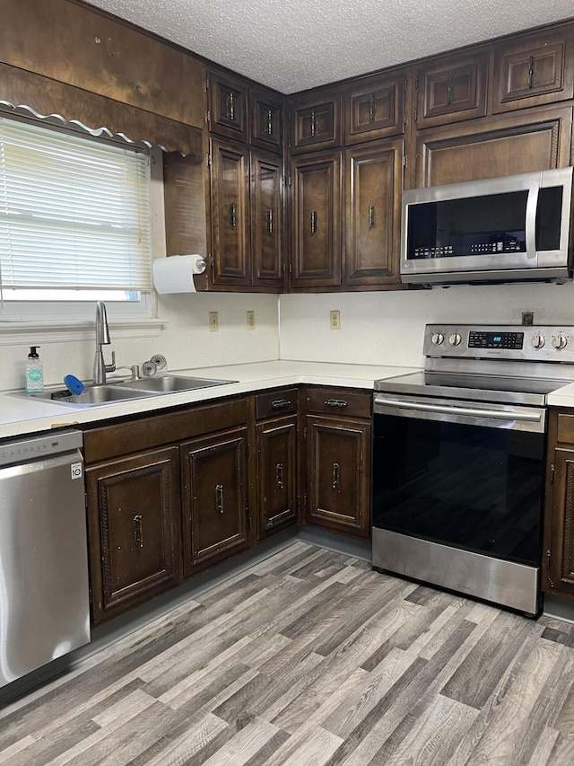 kitchen with a sink, light countertops, appliances with stainless steel finishes, a textured ceiling, and light wood-style flooring