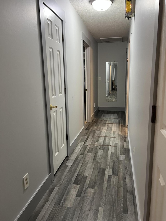 corridor with dark wood-style floors, baseboards, and a textured ceiling