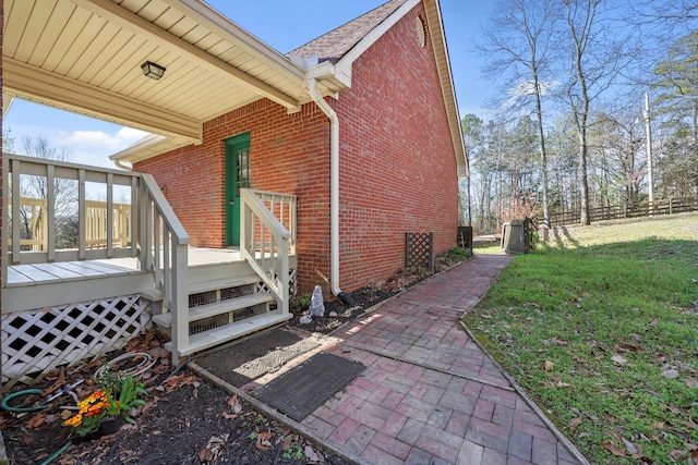 view of home's exterior featuring brick siding, fence, a deck, and a yard