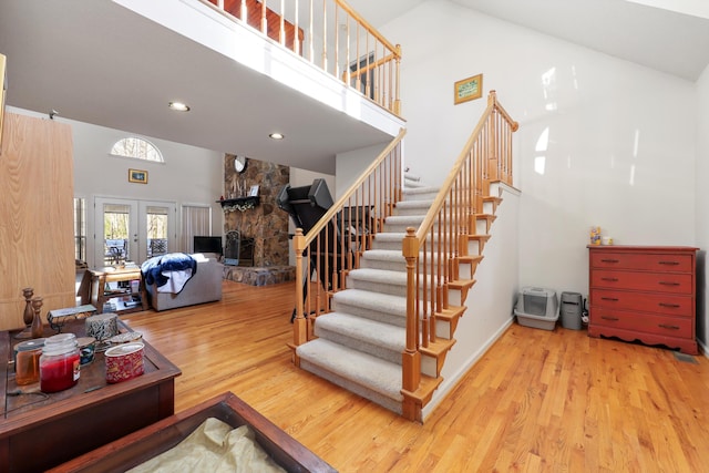 staircase with recessed lighting, a towering ceiling, wood finished floors, and a fireplace