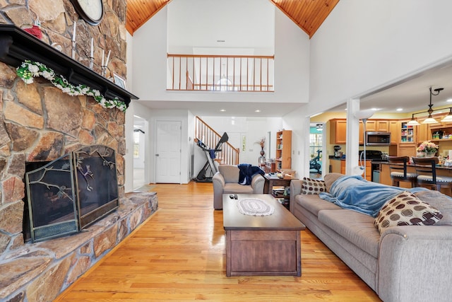 living area with a stone fireplace, vaulted ceiling, stairway, light wood-style flooring, and wood ceiling