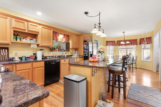 kitchen with light wood-type flooring, a kitchen breakfast bar, a kitchen island, black appliances, and a sink