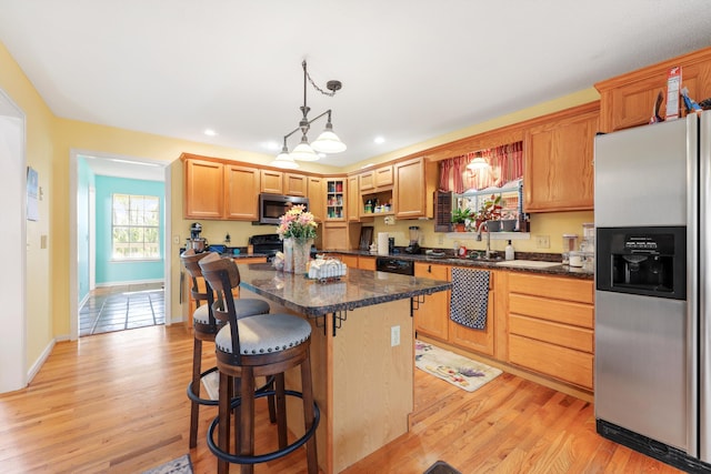 kitchen featuring a sink, light wood-style flooring, black appliances, and a kitchen breakfast bar