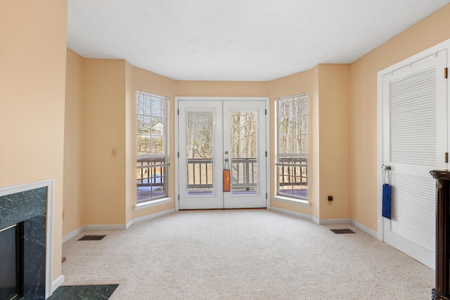unfurnished living room featuring visible vents, carpet floors, a premium fireplace, french doors, and baseboards