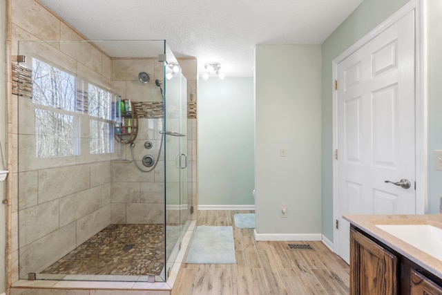 bathroom featuring vanity, baseboards, a textured ceiling, a shower stall, and wood tiled floor