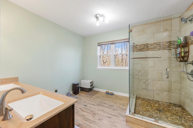 bathroom featuring a textured ceiling, vanity, wood finished floors, a stall shower, and baseboards