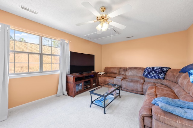 living area with ceiling fan, a textured ceiling, light colored carpet, visible vents, and attic access