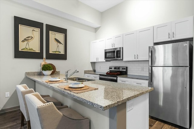 kitchen featuring backsplash, white cabinets, a kitchen bar, stainless steel appliances, and a sink