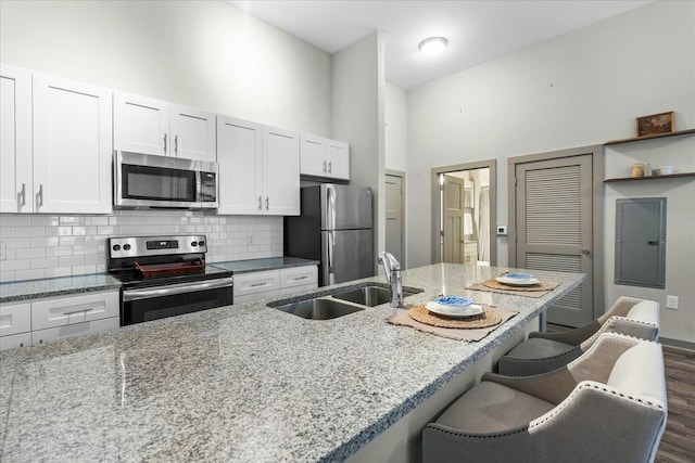 kitchen featuring backsplash, light stone countertops, a kitchen bar, appliances with stainless steel finishes, and a sink