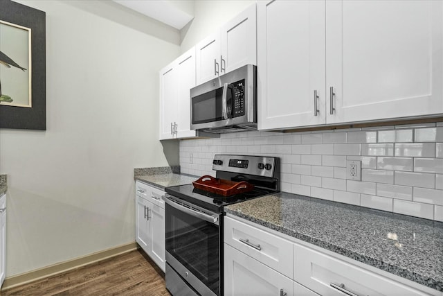 kitchen with dark wood-style flooring, backsplash, dark stone counters, and appliances with stainless steel finishes