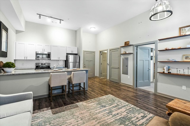 kitchen featuring a kitchen breakfast bar, white cabinets, appliances with stainless steel finishes, dark wood-style flooring, and decorative backsplash